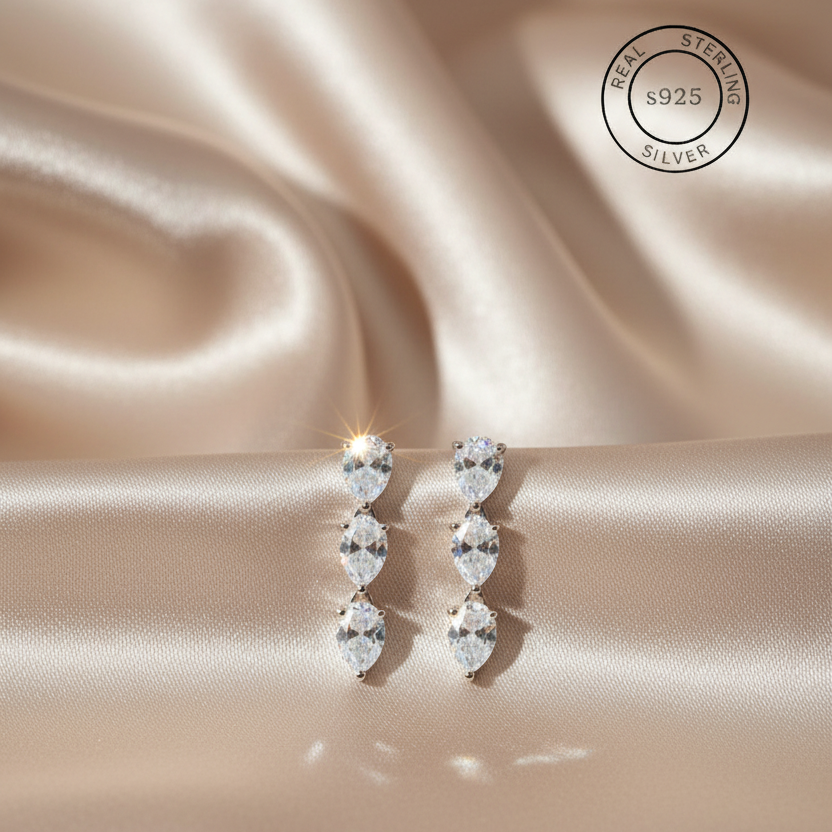 Pair of silver earrings with clear stones on a satin surface, featuring a 'Real Sterling Silver S925' stamp.