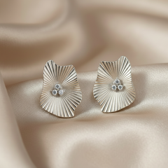 Pair of silver earrings with a textured design on a beige fabric background