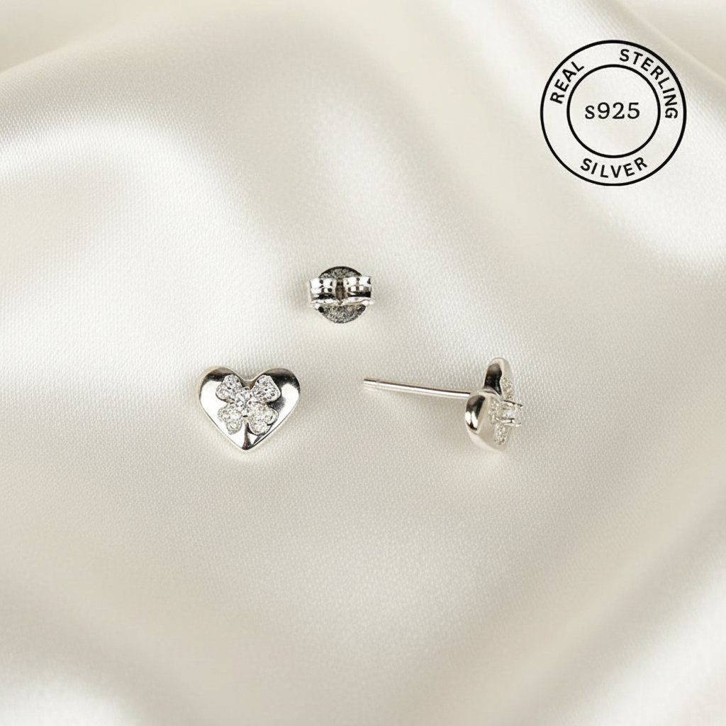 Heart-shaped silver earrings on a white satin background with 'Real Sterling Silver 925' stamp.