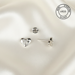 Heart-shaped silver earrings on a white satin background with 'Real Sterling Silver 925' stamp.