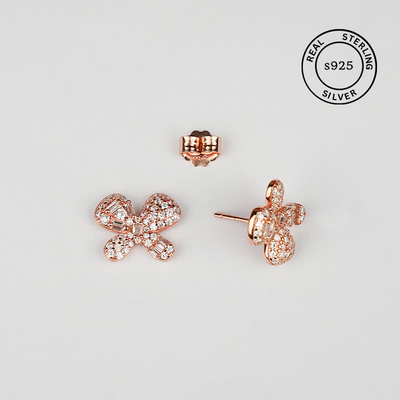 Rose gold bow-shaped earrings on a light gray background with 'Real Sterling Silver' stamp.