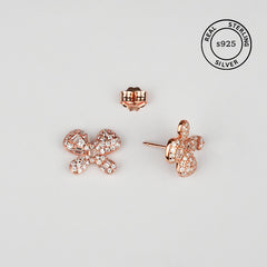 Rose gold bow-shaped earrings on a light gray background with 'Real Sterling Silver' stamp.