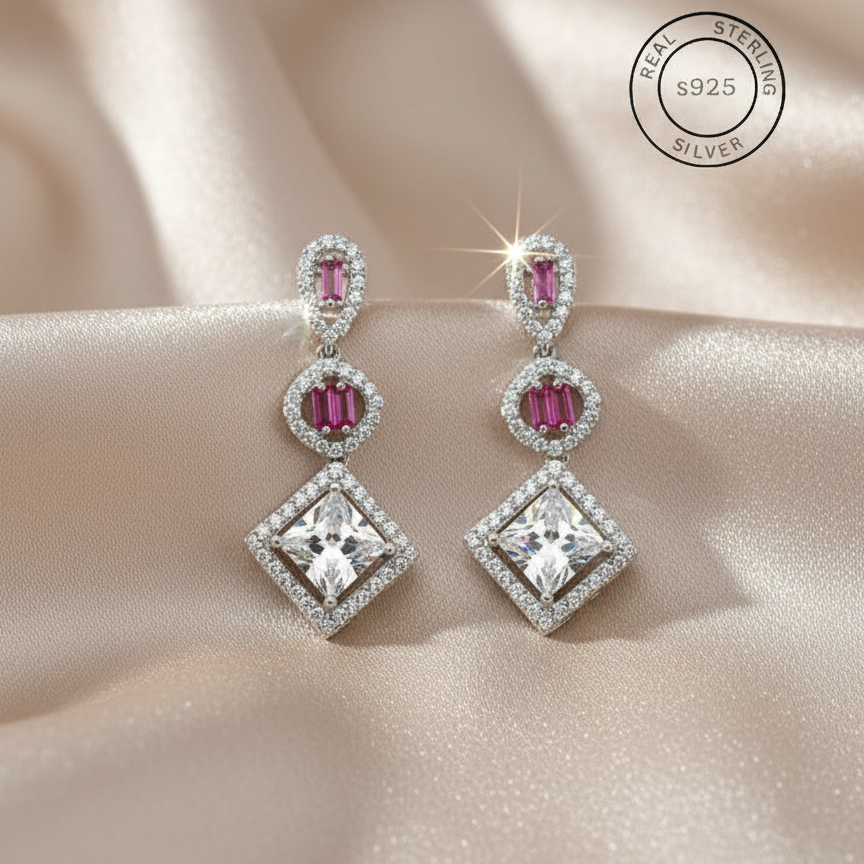 Pair of silver earrings with pink gemstones on a beige fabric background, featuring 'Real Sterling Silver' certification.