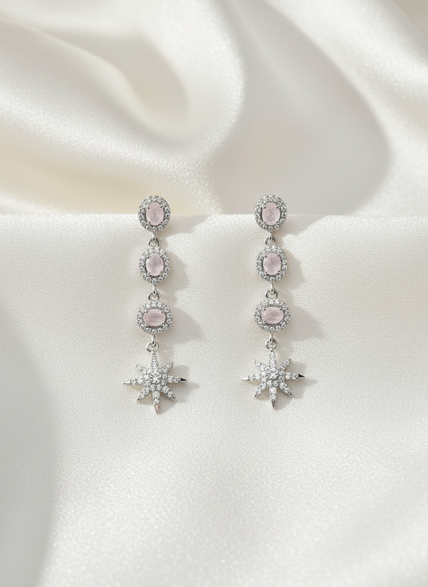 Pair of silver earrings with pink gemstones on a white fabric background