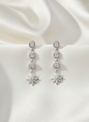 Pair of silver earrings with pink gemstones on a white fabric background