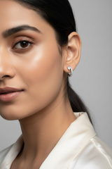 A close-up of a person's ear wearing a small silver huggie hoop earring adorned with clear stones.