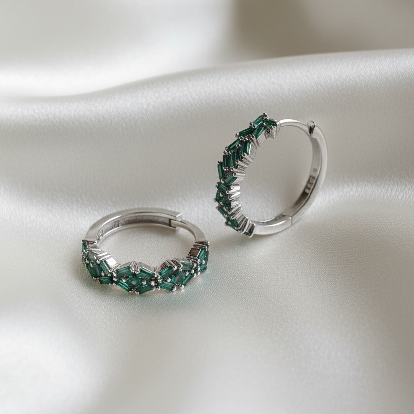 Silver hoop earrings with green gemstones on a white fabric background