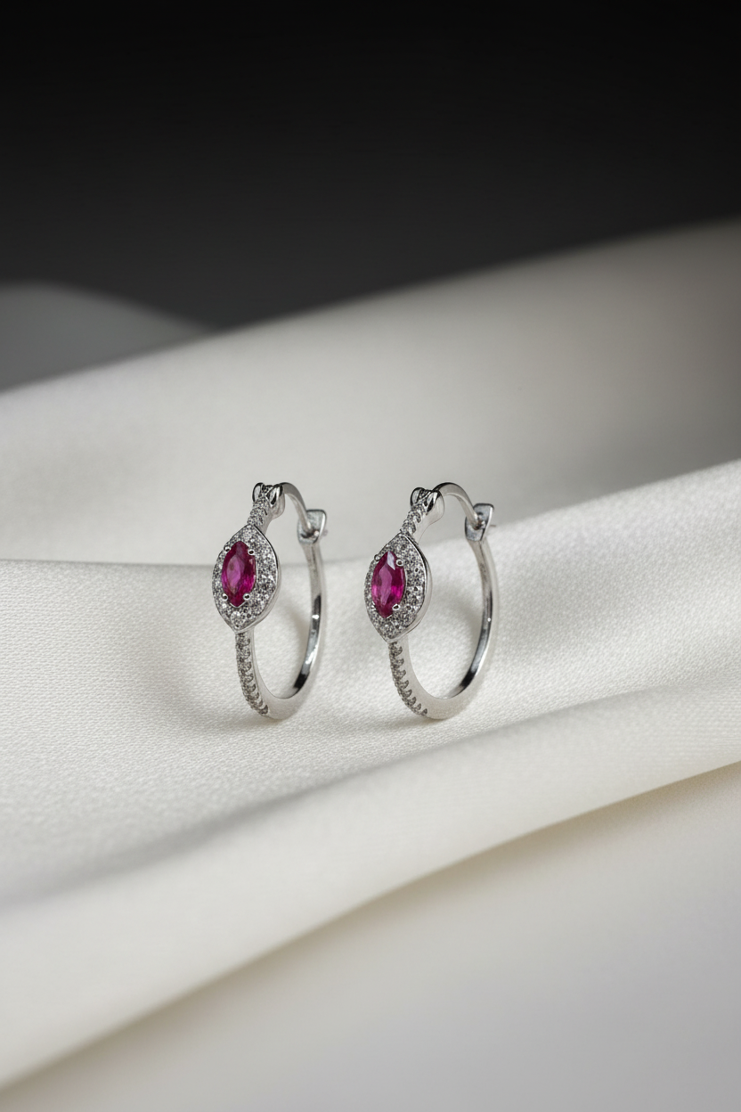 Silver hoop earrings with pink gemstones on a white fabric background
