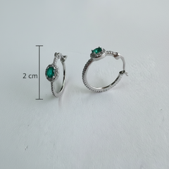 Silver hoop earrings with green gemstones on a light gray background