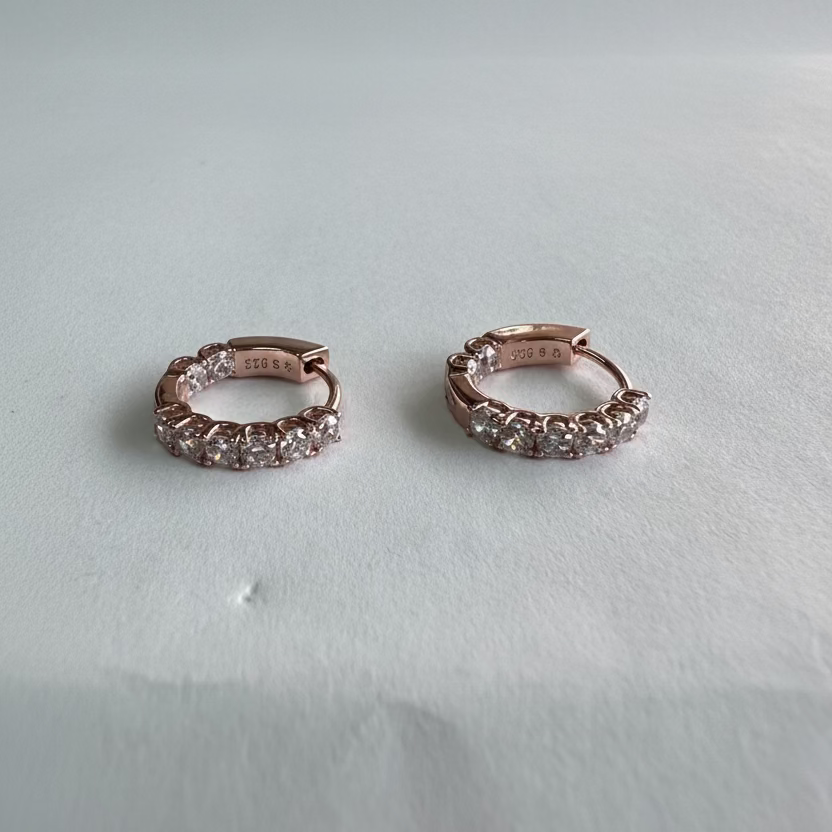Rose gold hoop earrings with gemstones on a light gray background