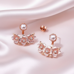 Rose gold floral earrings with pearls on a soft pink fabric background