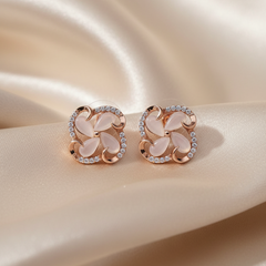 Pair of rose gold earrings with pink stones on a beige fabric background