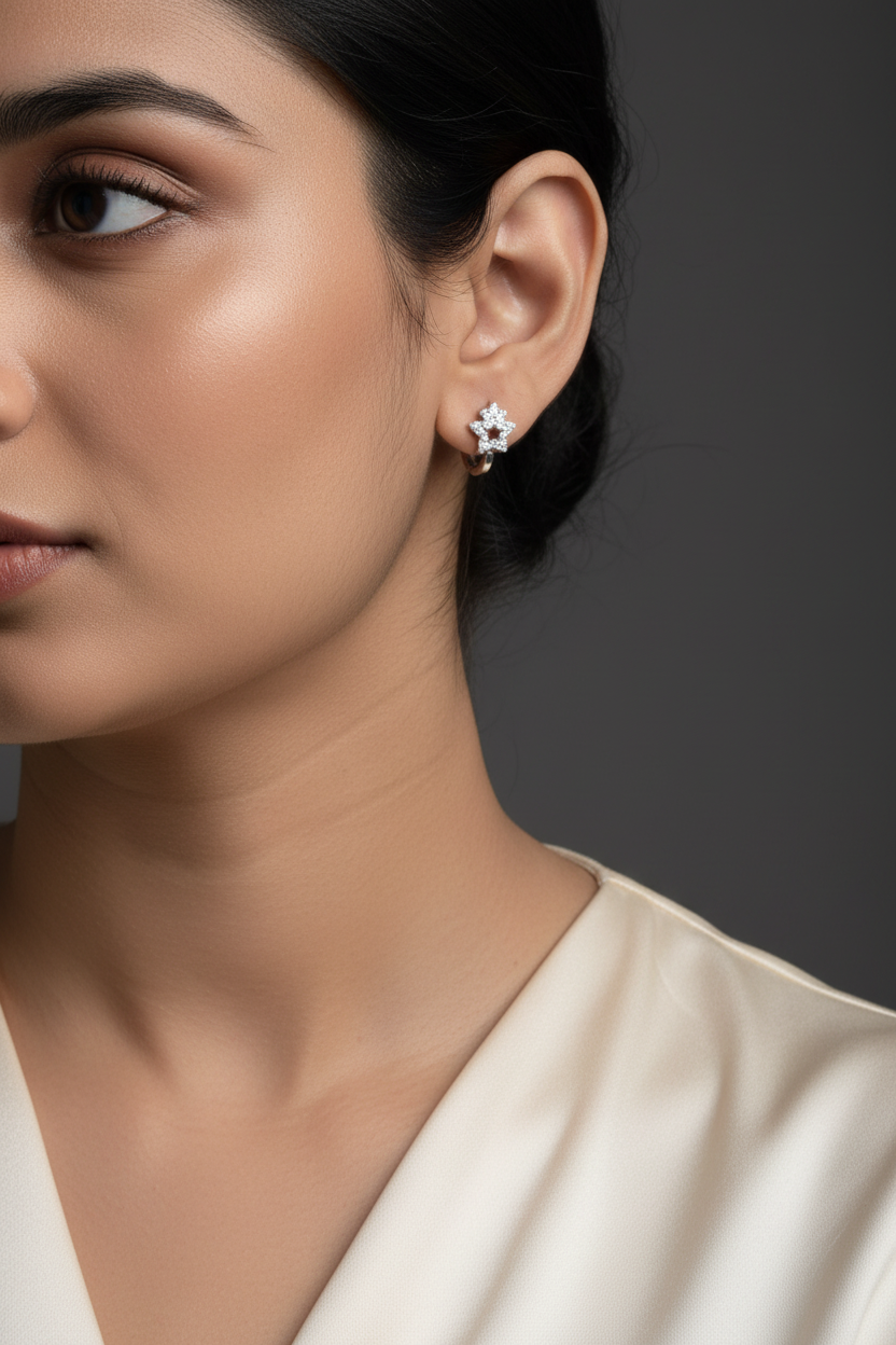 A close-up side profile of a person's ear wearing a small silver-toned star-shaped stud earring with clear stones.