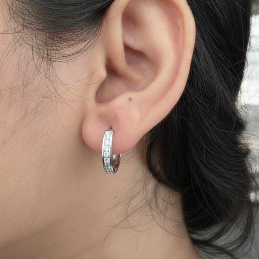 Close-up of an ear wearing a silver hoop earring with small stones.