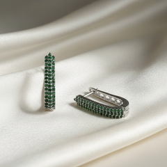 Pair of green gemstone hoop earrings on a white fabric background